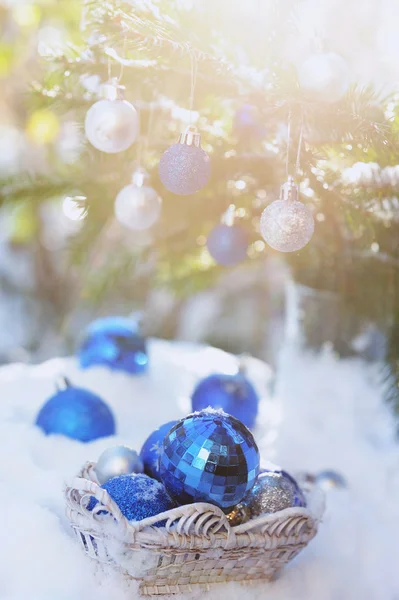 White basket with xmas balls on the snow and blue balls on christmas tree
