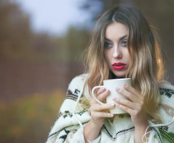 Young beautiful blonde woman with cup of coffee standing by the window