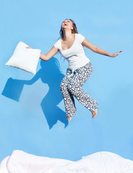 Woman holding a pillow jumping up on bed