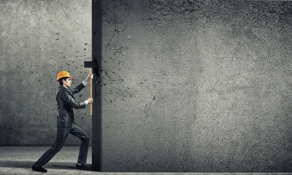 Businessman in helmet breaking wall