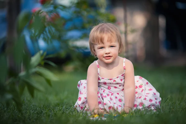 Baby girl with blue eyes and blond hair plays toy on the grass