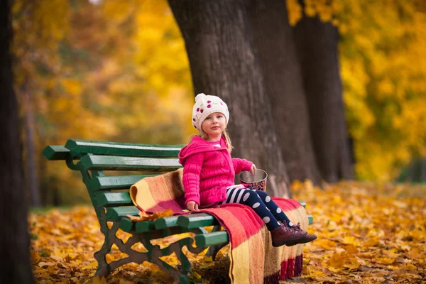 Little girl on the bench in the autumn garden