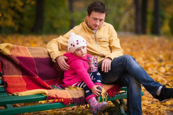 Father and daughter sits on the bench in autumn garden
