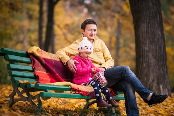 Father and daughter sits on the bench in autumn garden