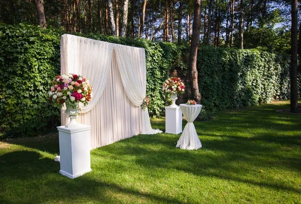 Wedding arch with big flower bouquets on the green leaves backgr