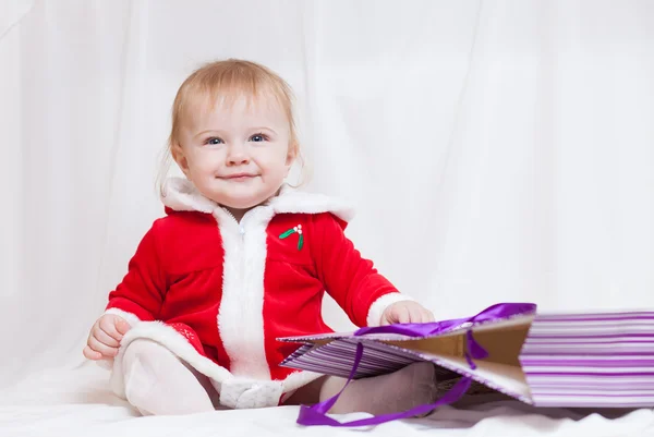 A little baby-girl dressed red fancy Santa Claus dress with violet paper-bag for gifts
