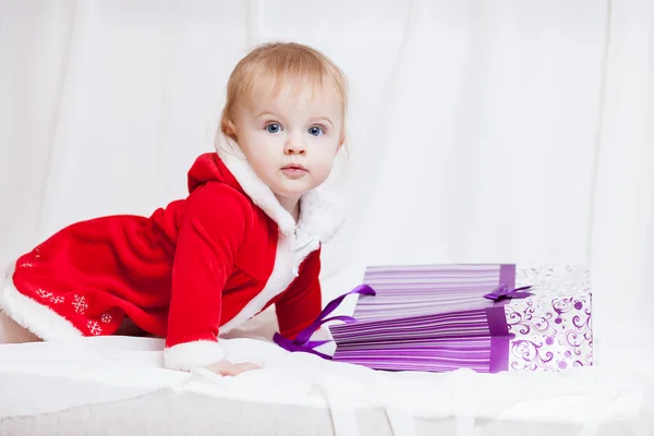 A little baby-girl dressed red fancy Santa Claus dress with violet paper-bag for gifts