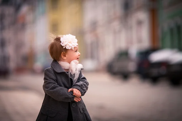 A portrait of little baby girl in gray coat on the street in old city with funny smile