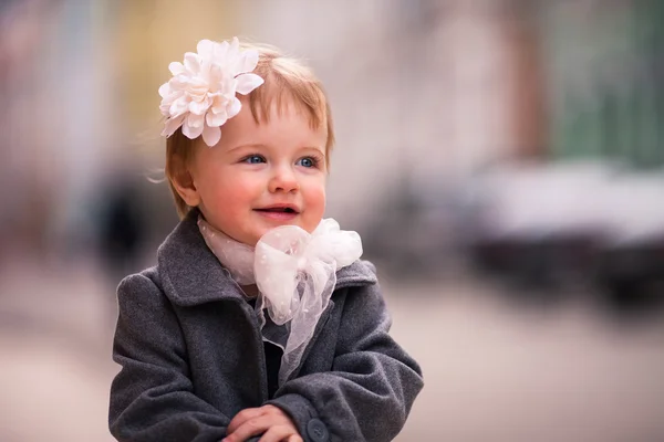 A portrait of cute little baby girl in gray coat on the street in old city with funny smile