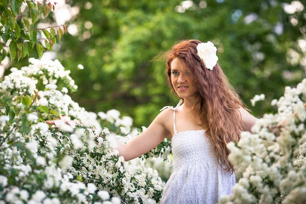 Charming young lady with beautiful smile in spring garden full of white flowers