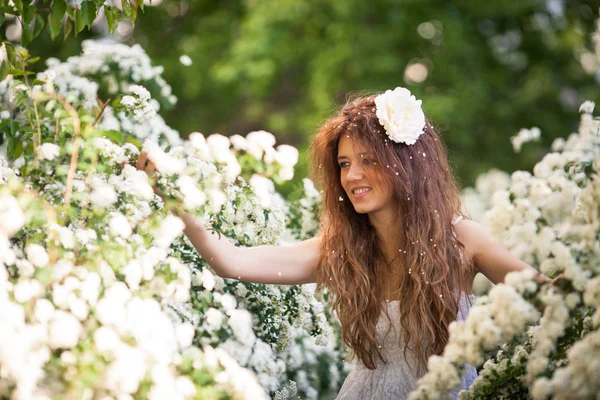 Charming young lady with beautiful smile in spring garden full of white flowers