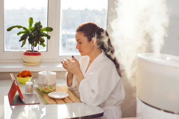 Woman drinking tea reading tablet at humidifier