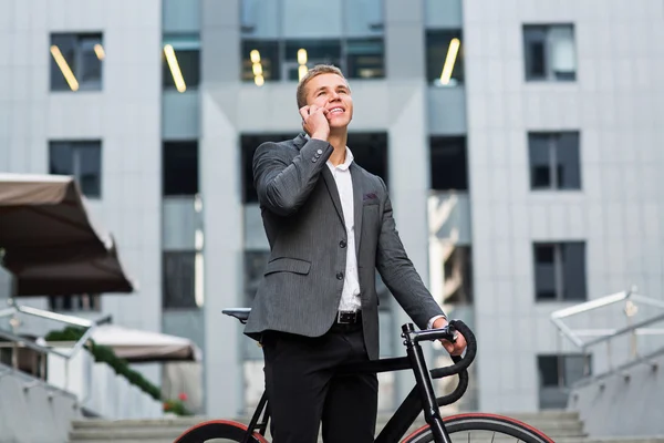 A young businessman standing on the steps of an office building, with a folder of papers and bike.Young handsome businessman talking on mobile phone