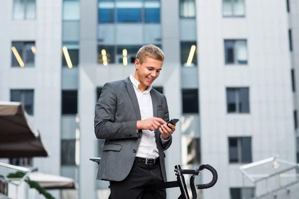 A young businessman standing on the steps of an office building, with a folder of papers and bike.Young handsome businessman talking on mobile phone