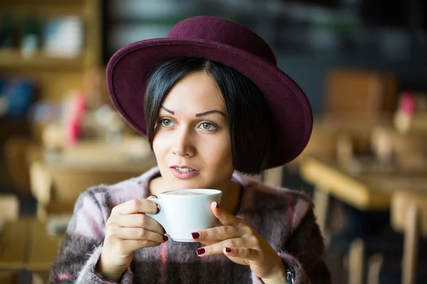 Girl in Cafe holding cup of hot coffee in hand, smiling