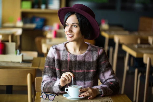 Girl in Cafe holding cup of hot coffee in hand, smiling