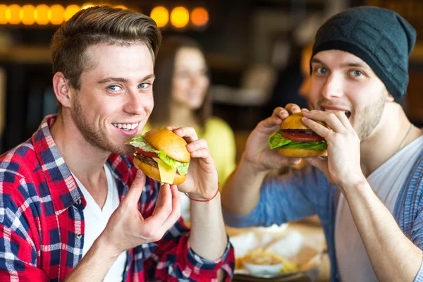 Two man eating burger. Young girl and young man are holding burgers on hands
