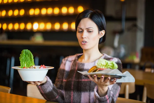 Woman holding a salad and a burger.Woman choosing between healthy and unhealthy eating