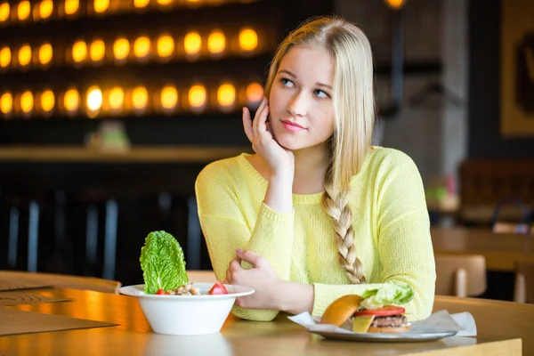 Woman holding a salad and a burger.Woman choosing between healthy and unhealthy eating