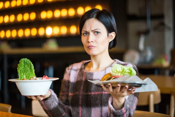 Woman holding a salad and a burger.Woman choosing between healthy and unhealthy eating