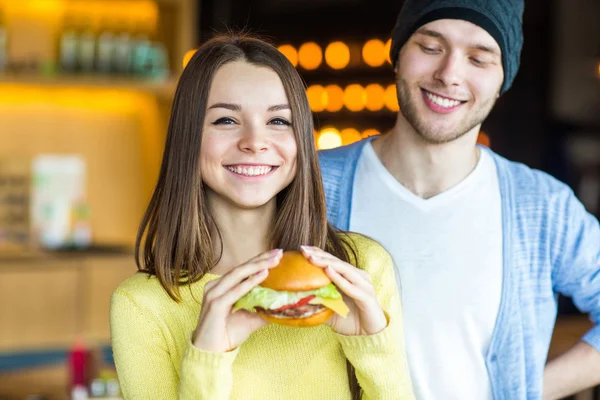 Man and woman eating burger. Young girl and young man are holding burgers on hands