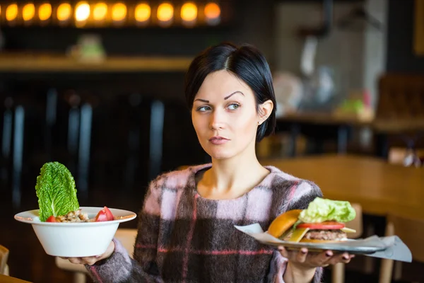 Woman holding a salad and a burger.Woman choosing between healthy and unhealthy eating