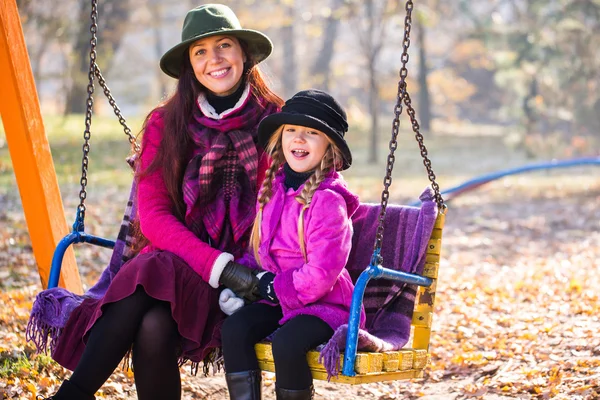 Happy mother and daughter ride on a swing in the autumn park. mother and daughter in the autumn park