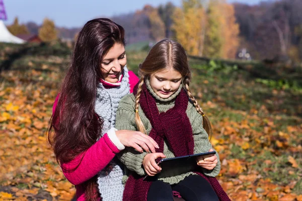 Mother and daughter with tablet in the autumn park on a bench.Mom and daughter in the park