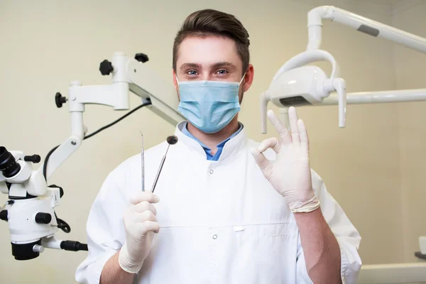 People, medicine, stomatology and healthcare concept - happy young male dentist with tools over medical office background