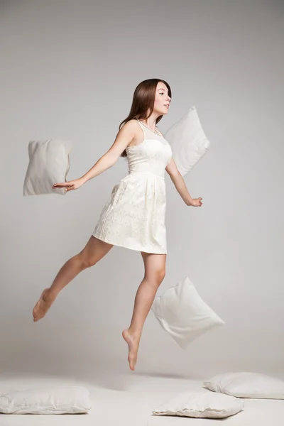 Woman in white dress in mid air with flying pillows