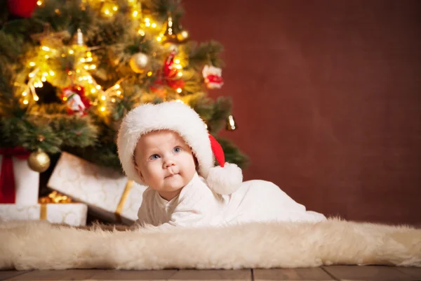 Happy baby wearing Santa hat over christmas tree