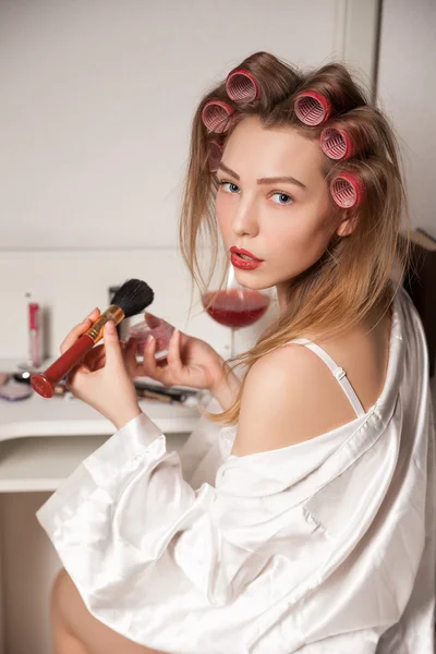 Young woman with curler hair doing make up behind mirror