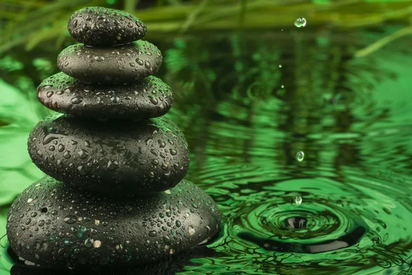Pyramid made of stones and a drop in the green water