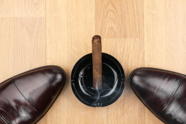 Classic men's shoes, ashtray and  fuming cigar on the wooden floor