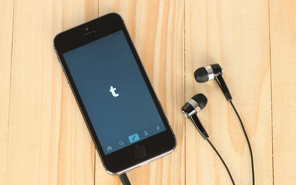 IPhone with Tumblr logotype on its screen and headphones on wooden background