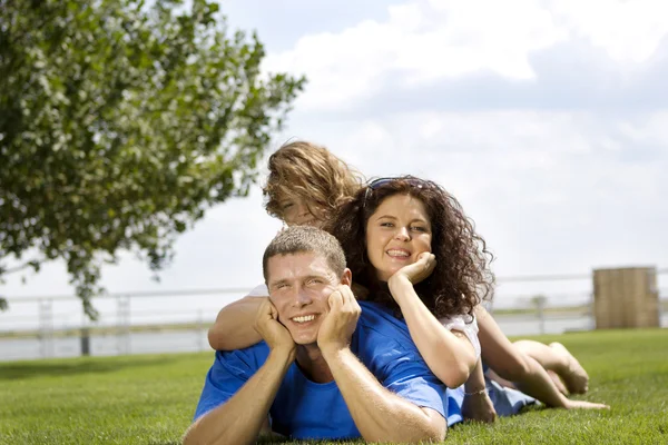 Happy beautiful young family lying on the green grass. Three cheerful person