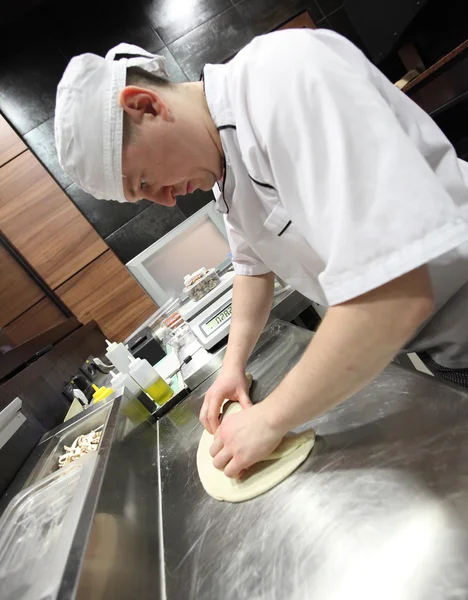 Chef baker in white uniform making pizza at kitchen.Focus on the hands
