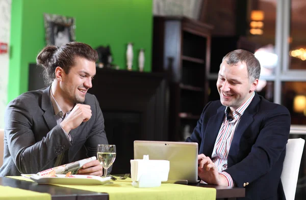 Two smiling business men eat at restaurant
