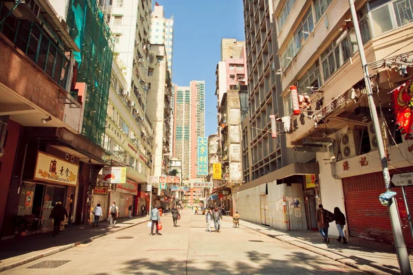 People walking on sunny street with tall concrete buildings in Hong Kong.