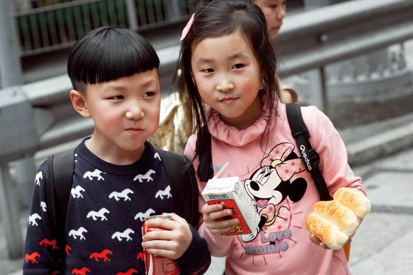 Unidentified boy and girl eating snacks outdoor on the way from school