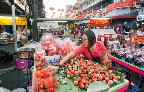 Strawberry saleswoman arranges items on the counter of vibrant street market