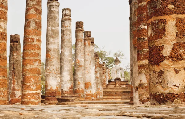 Columns of ancient ruined temple Wat Maha That with back of stone Buddha statues at Sukhothai historical park