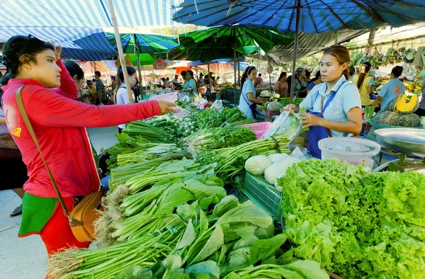Woman buying green vegetables at village market with fresh farmers food