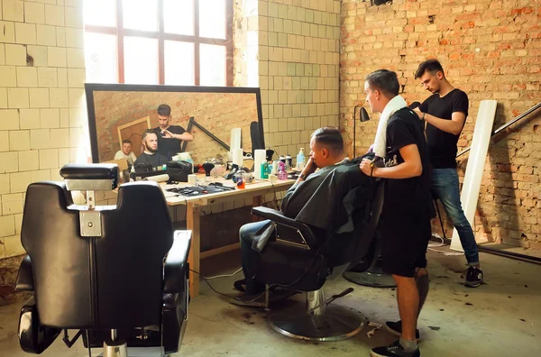 Young guys making haircuts in the hipster style barber shop with grunge walls