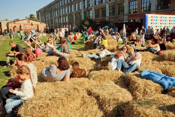 People and young families relaxing in the hay on the ground of outdoor city festival