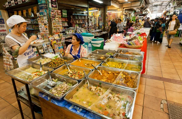 Two women sell asian fast-food with meat inside the market with delicacies and farming products