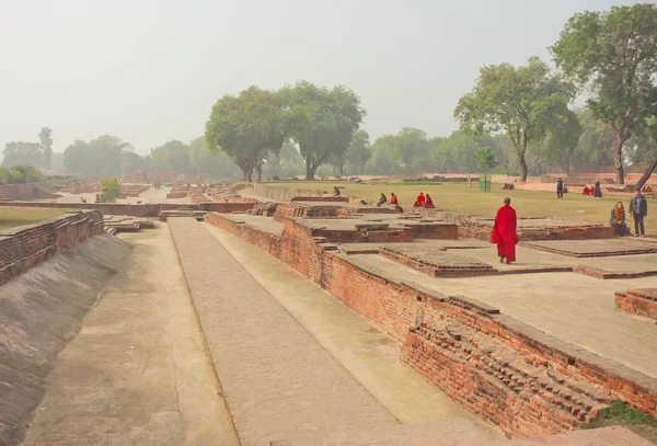 Buddhist monk in red dress walking past ruined temple in sacred place with green trees