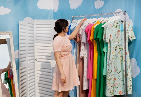 Beautiful woman making choice in showroom of bright fashion store