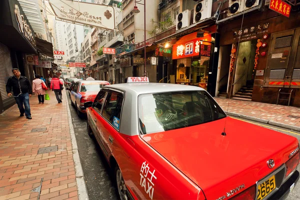Taxi cars waiting for the passengers on busy city street with many stores in Hong Kong.