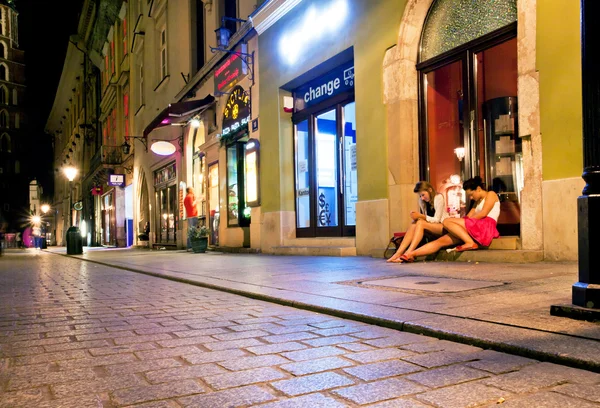 Young women sit on the groung on the night street of old city with bars & cafes.